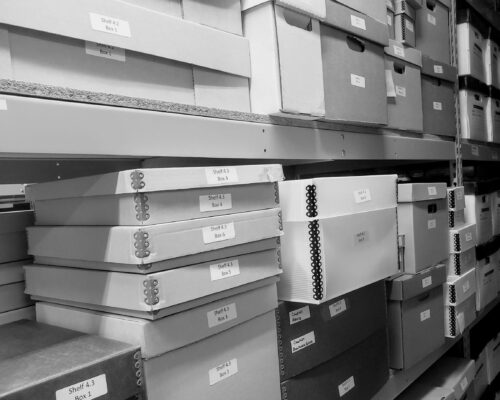 Archival Boxes Black, white, and grey archival boxes stacked on shelves.