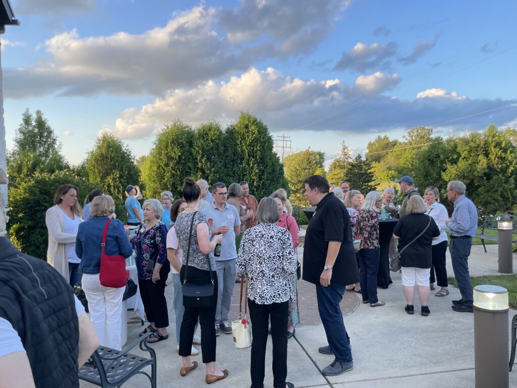 Group of people standing outside talking underneath a cloudy blue sky in front of trees
