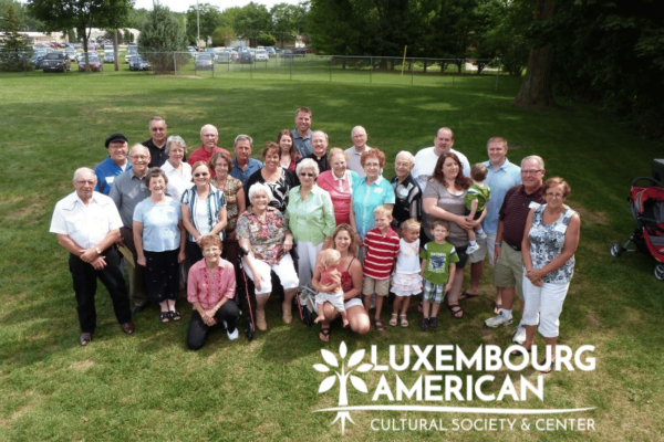 Family posing for a photo on a grass field with trees and cars in the background