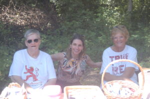Three women smiling, sitting in a half shaded half sunny spot